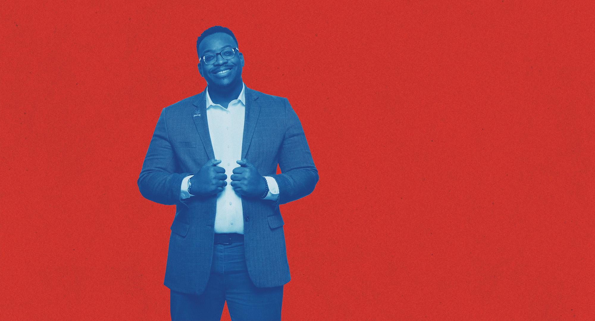 在线博彩 Student dressed in a suit posing and smiling in front of a red background.